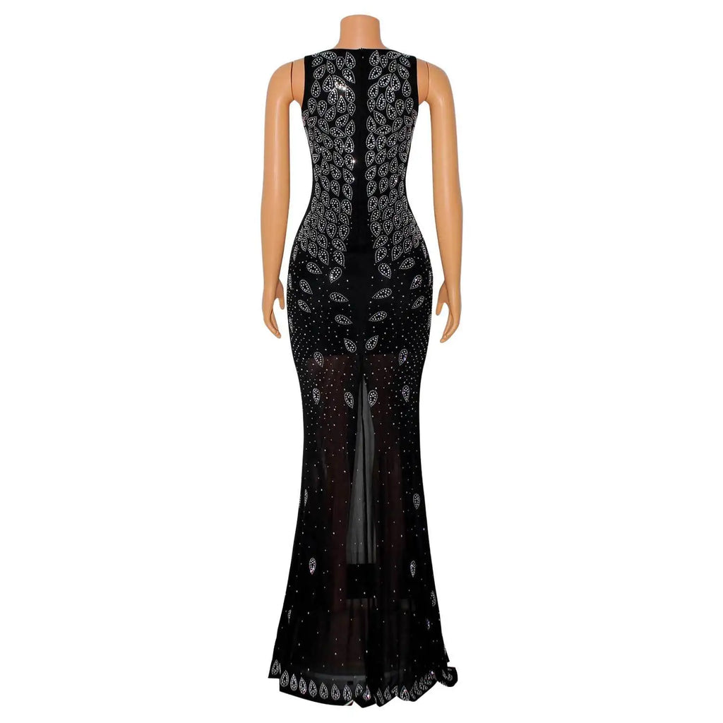 Black floor-length sheer mesh dress featuring intricate sparkling rhinestone patterns, a high back slit, and a sleeveless silhouette.