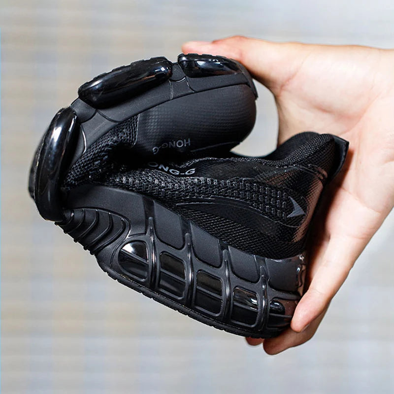 A hand holding a flexible, black work trainer, demonstrating its durable, puncture-proof sole and lightweight design.