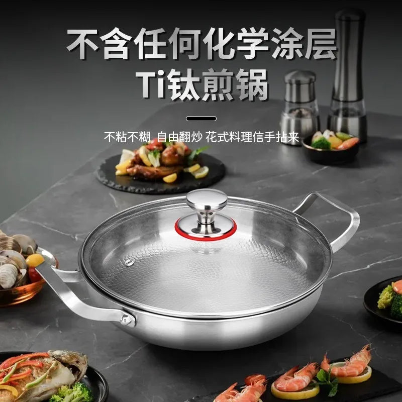 A stainless steel frying pan with a glass lid and two handles, placed on a dark surface with food around it.