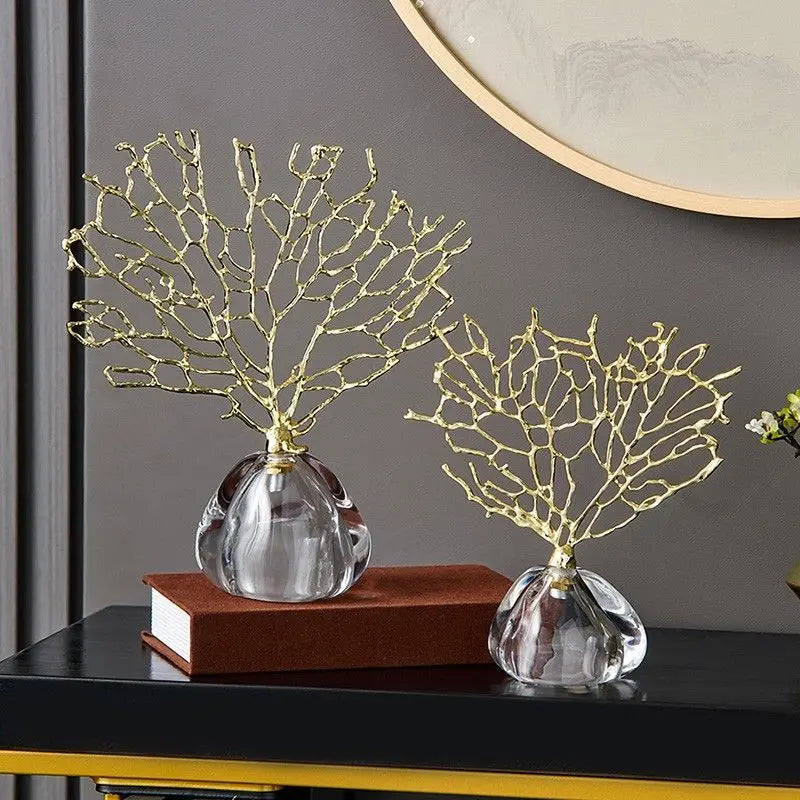 Two gold-branch sculptures on clear glass bases; one sits on a book.