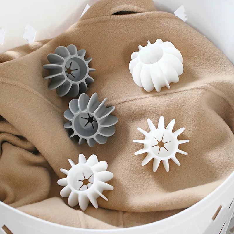 Set of white and grey silicone laundry dryer balls with star-shaped centres, resting on a folded camel-coloured jumper.