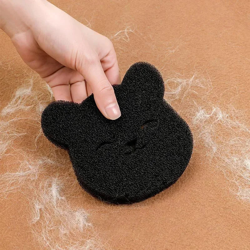 A black, bear-shaped foam sponge for removing pet hair from a brown fabric surface.