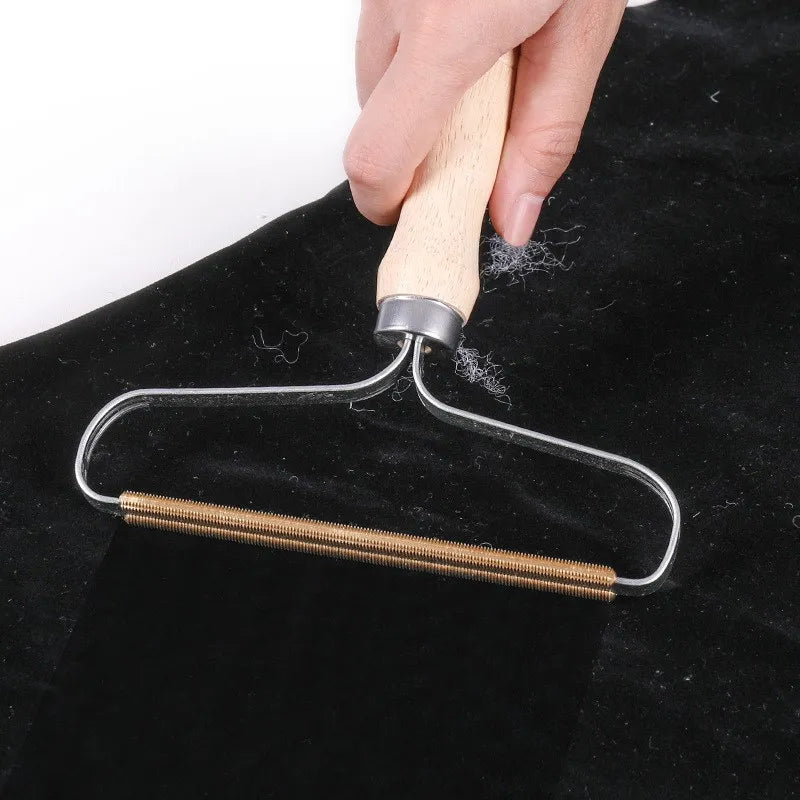 Handheld fabric lint remover with a wooden handle and copper-edged blade, removing bobbles from black fabric.