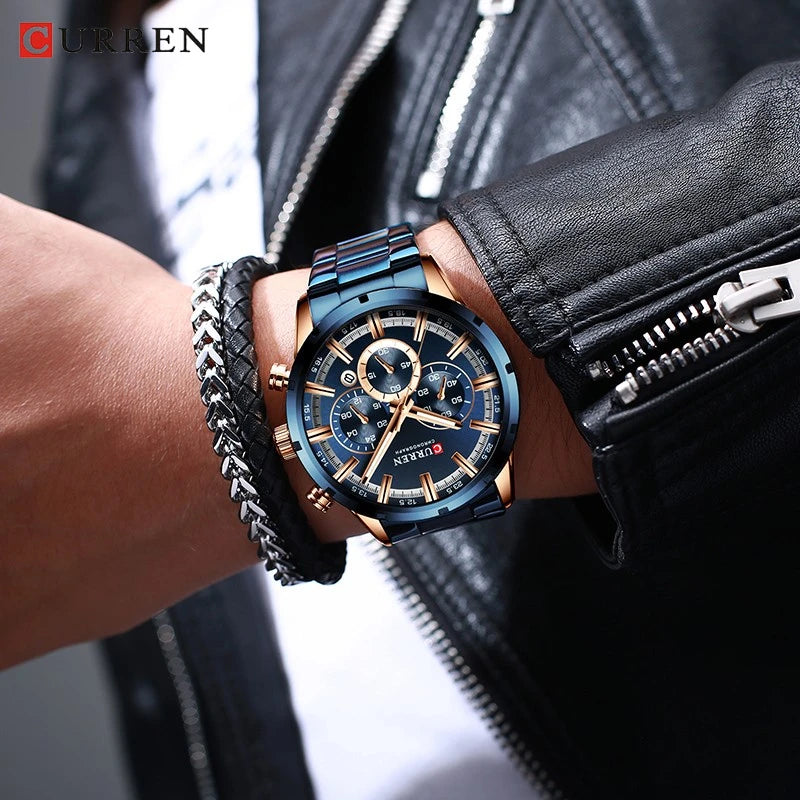 CURREN blue and gold chronograph watch with a round face, worn on a wrist with bracelets.