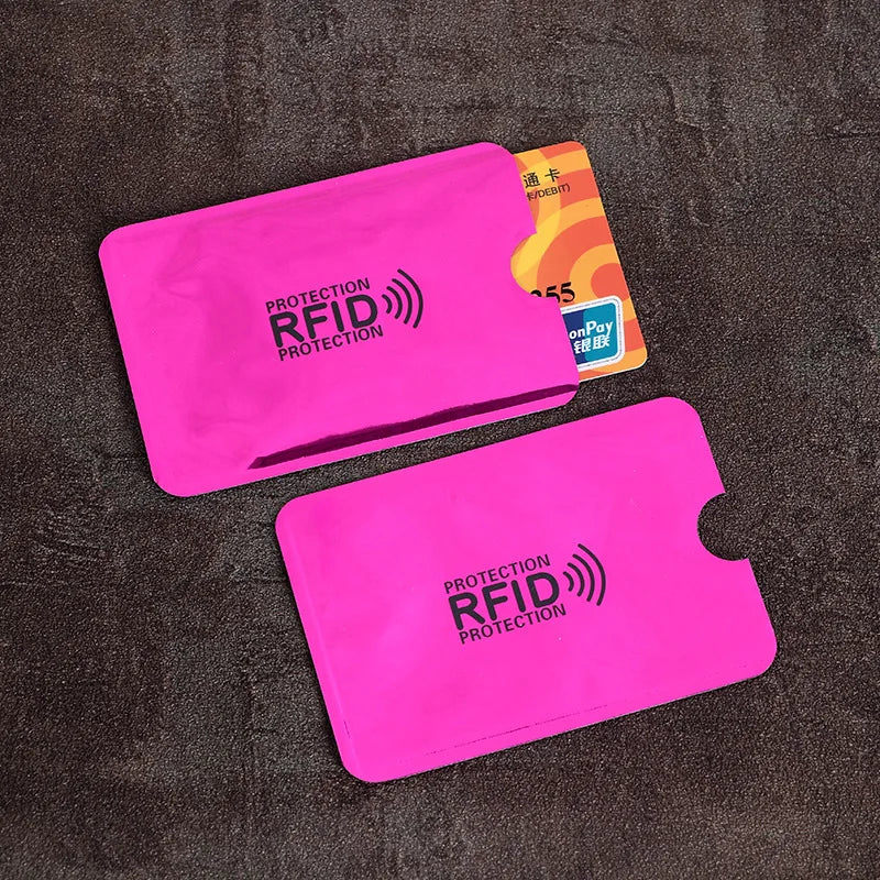 Two pink plastic RFID-blocking sleeves for credit cards on a dark textured background.