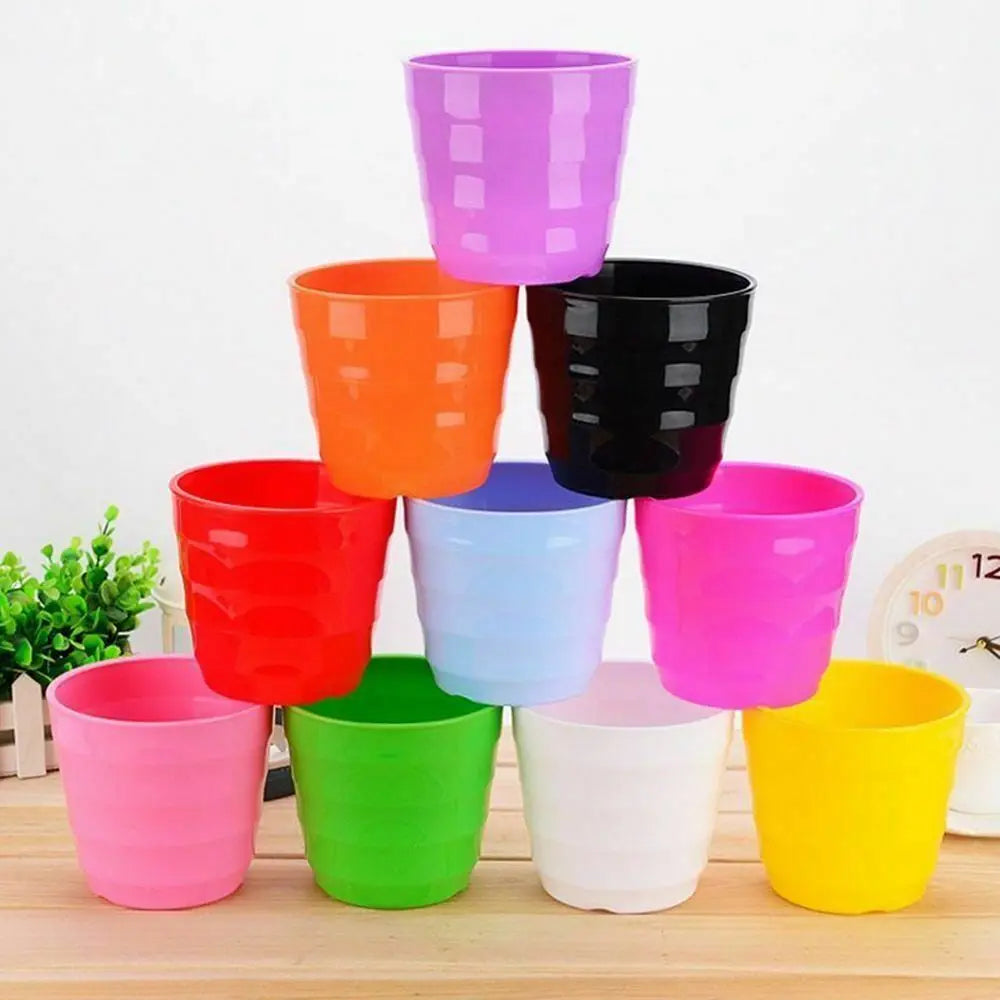 A pyramid stack of colorful, ridged plastic flower pots in various bright colors, set on a wooden table.
