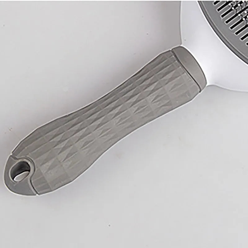 Close-up of a white and grey pet grooming brush with a textured, diamond-patterned handle and hanging loop.