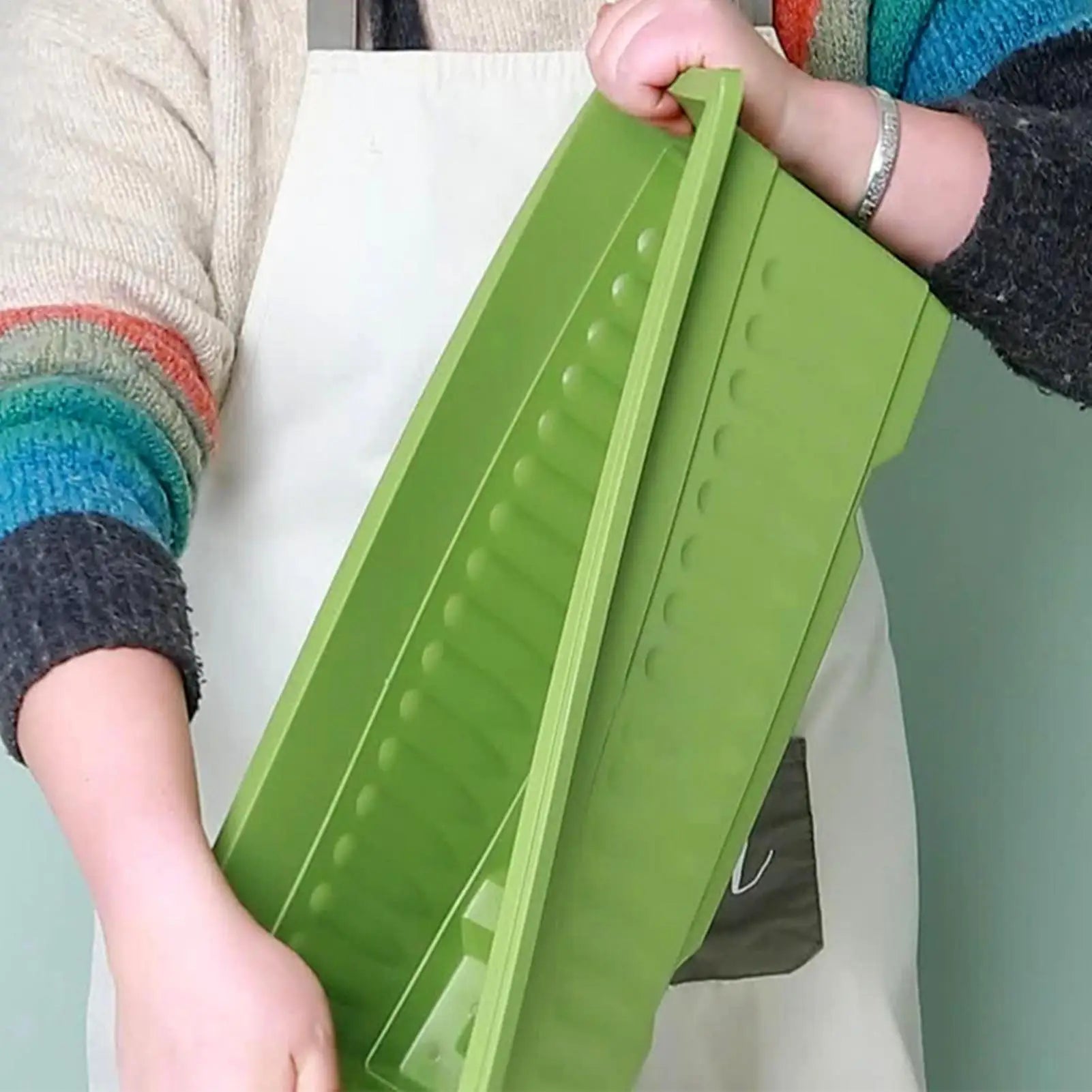 A person in an apron holds a long, rectangular lime-green plastic garden planter with ribbed decorative side detailing.