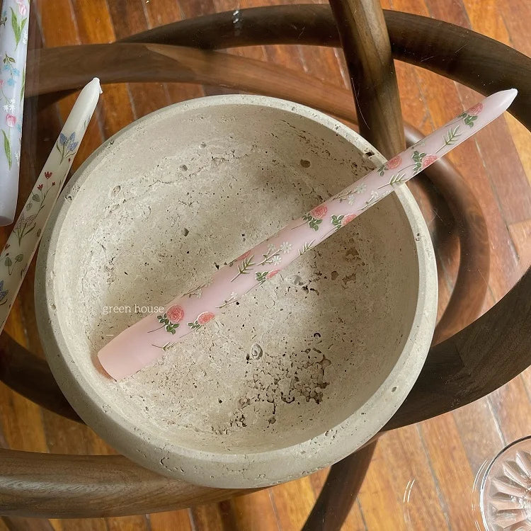 Slim pale pink tapered dinner candle featuring delicate floral and rosebud patterns, resting in a rustic stone bowl.