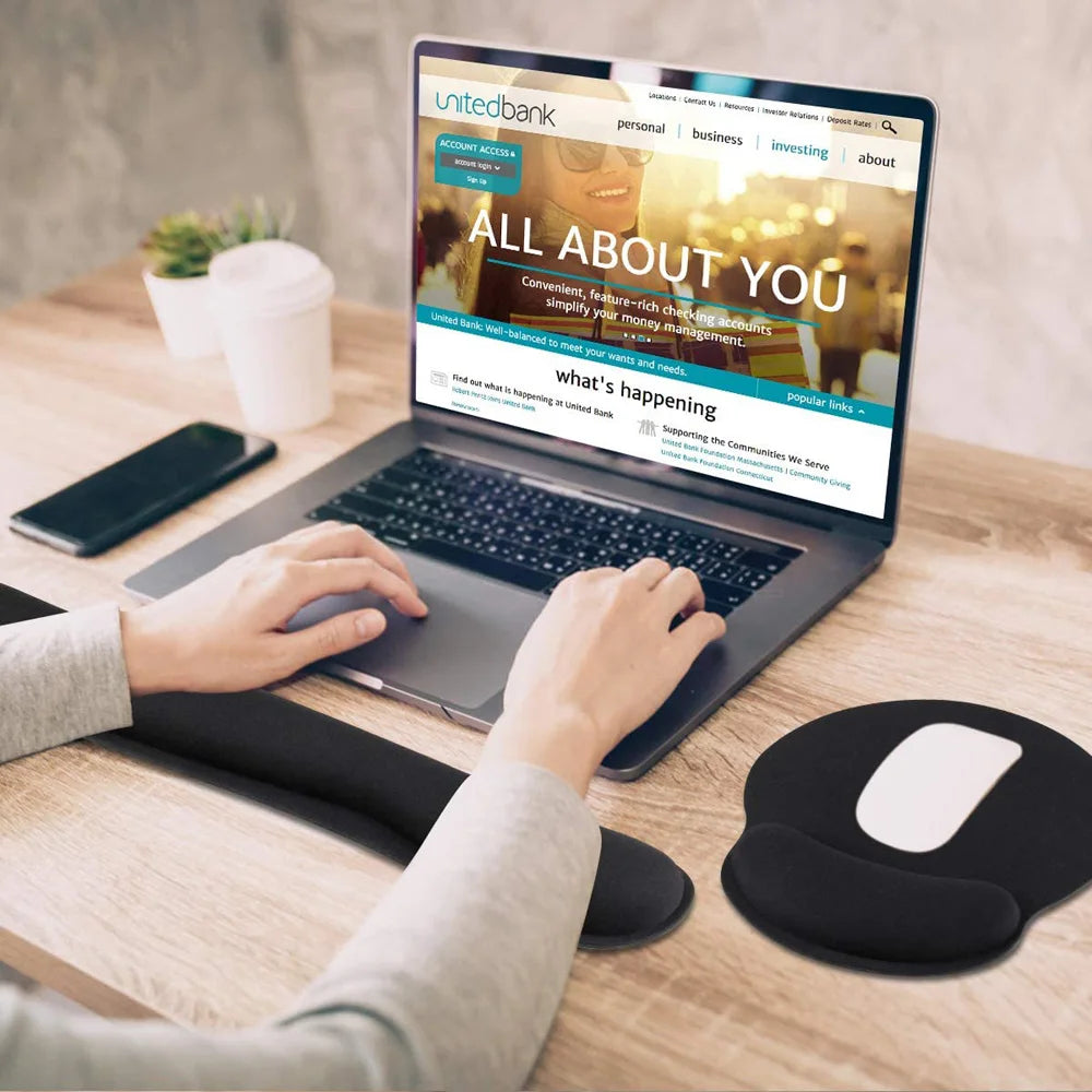 Black foam wrist rest and mouse pad set for ergonomic support on a wooden desk with a laptop.