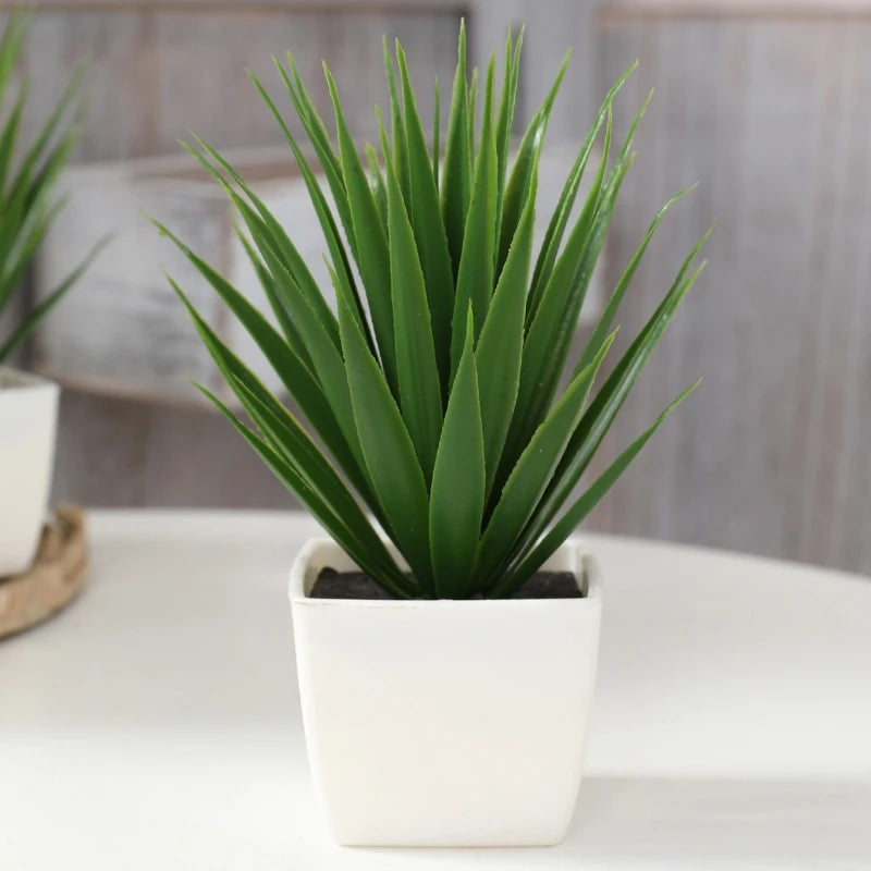 A vibrant green artificial agave-style plant in a modern, square white pot sitting on a white surface.