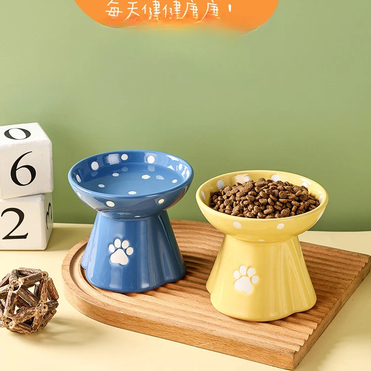 Two elevated ceramic cat bowls in blue and yellow, featuring white polka dots and paw print designs on a wooden tray.