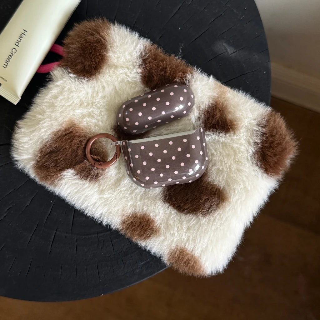 Brown polka dot AirPod Pro case in a hard plastic finish with a matching keyring, resting on a faux fur pouch.