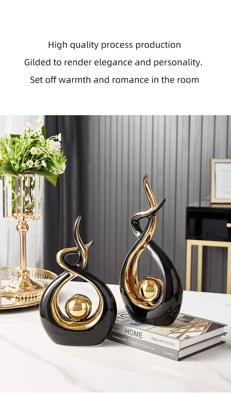 Two modern, abstract black and gold ceramic ornaments with curved, flame-like designs on a white table.