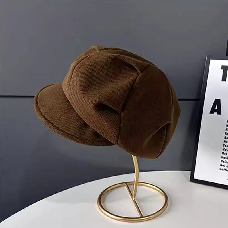 Dark brown textured retro newsboy beret hat with a structured peak, displayed on a gold stand.