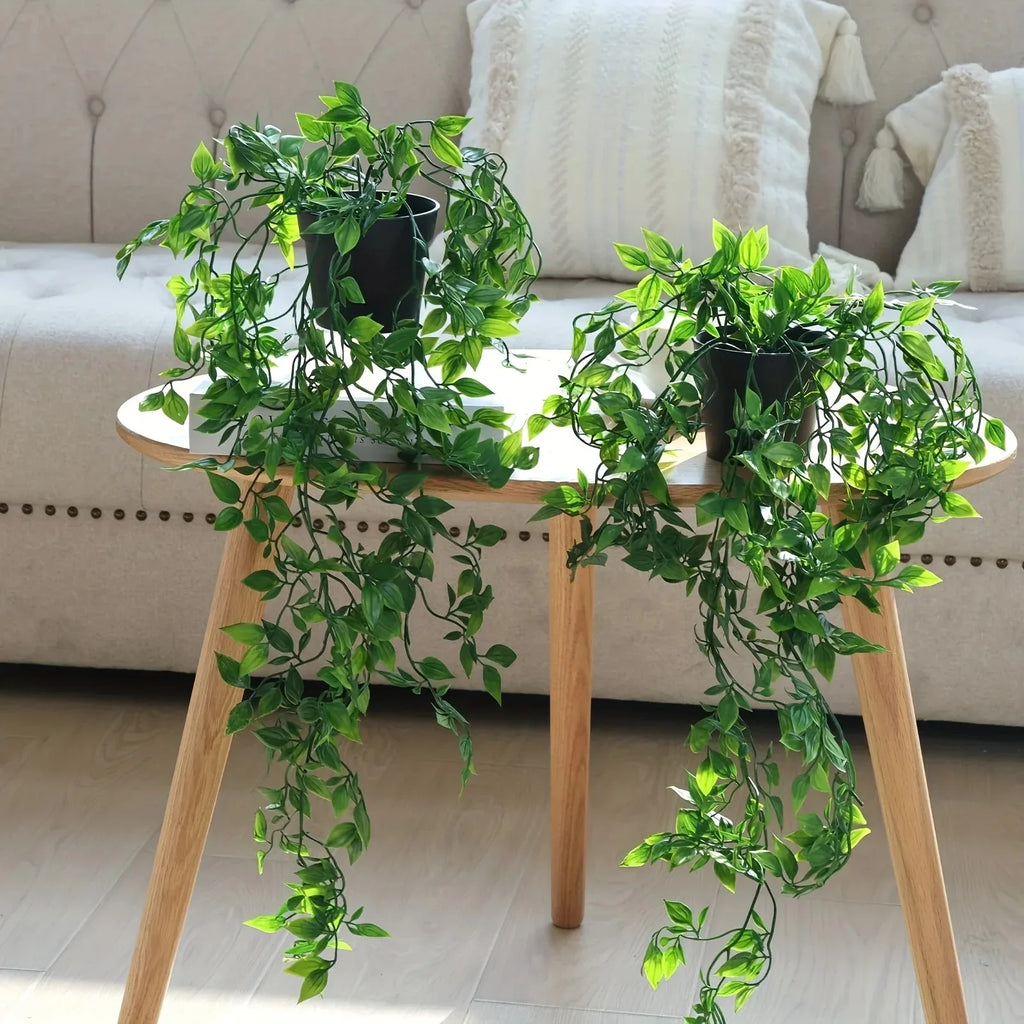 Two artificial cascading green ivy plants in black pots, sitting on a wooden side table in a bright, cozy living room.