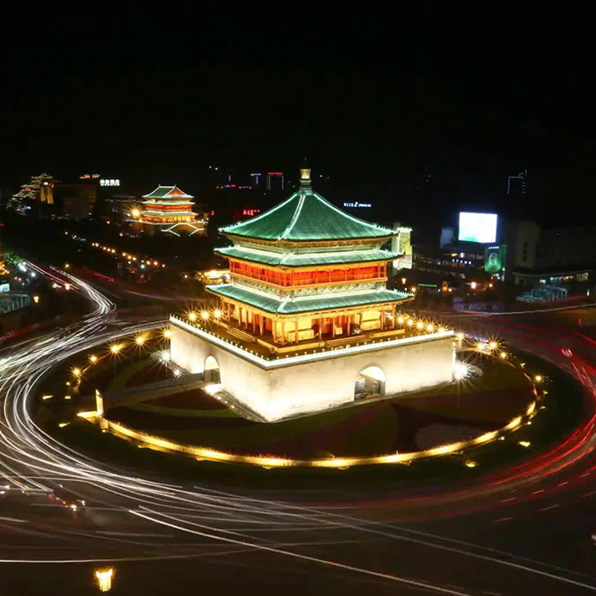 Night view of a traditional multi-tiered Chinese pagoda illuminated in gold and green, surrounded by city traffic trails.