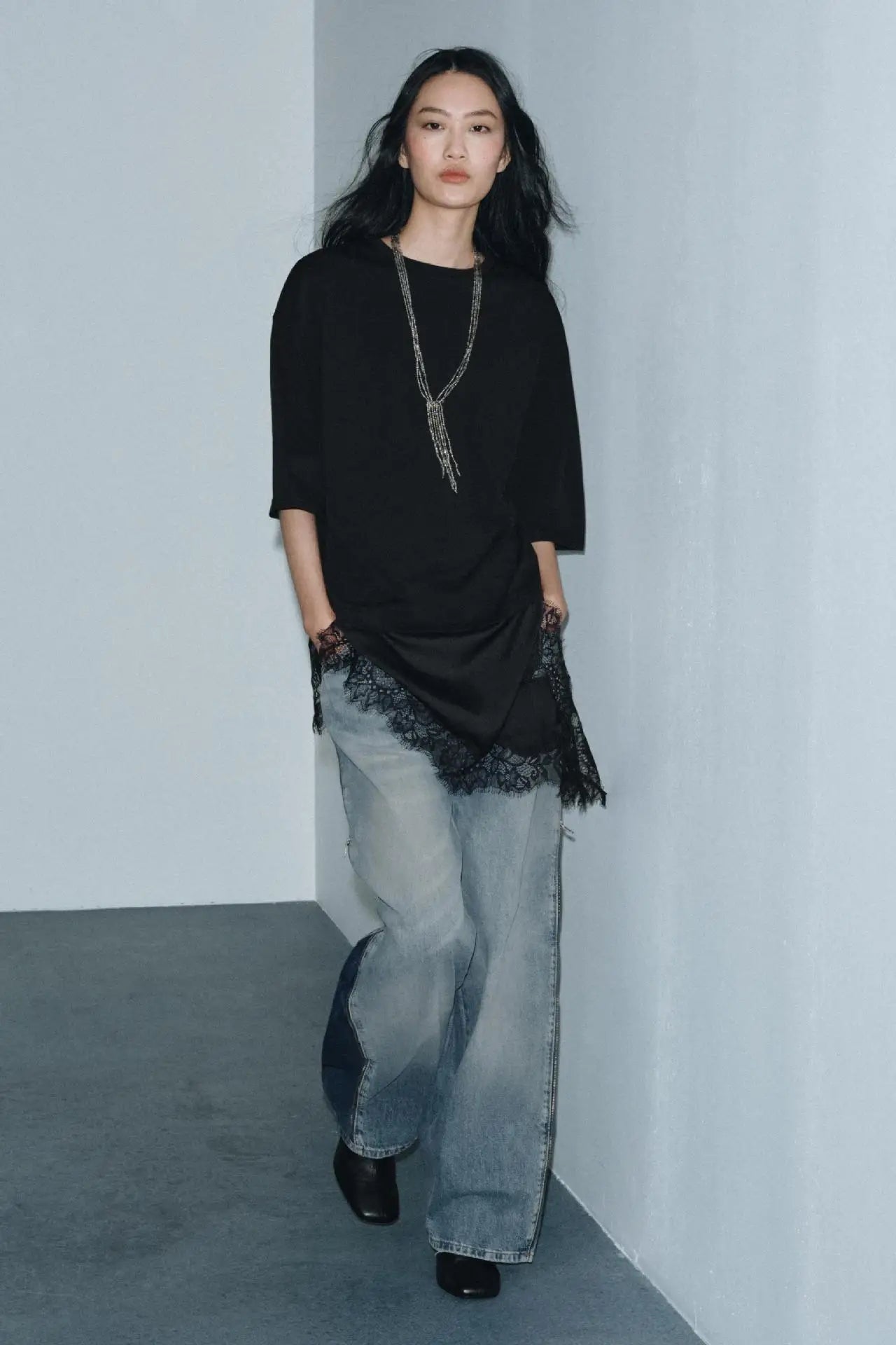 Model wearing a black oversized t-shirt with a lace hem, styled with loose-fit light blue denim jeans.