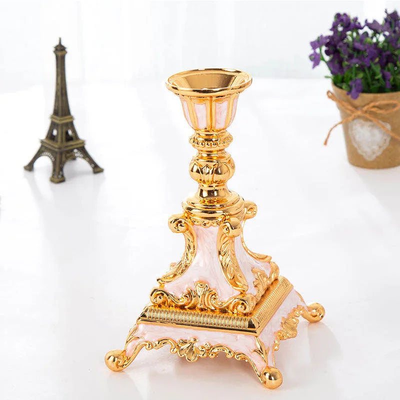 Gold and pink ornate metal candlestick with a wide square base and intricate scrollwork details.