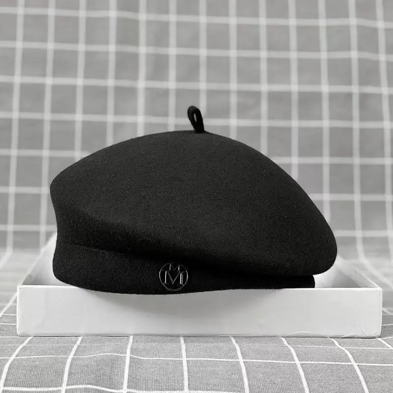 A classic black wool felt beret with a small top loop and a metallic circular detail on the front.