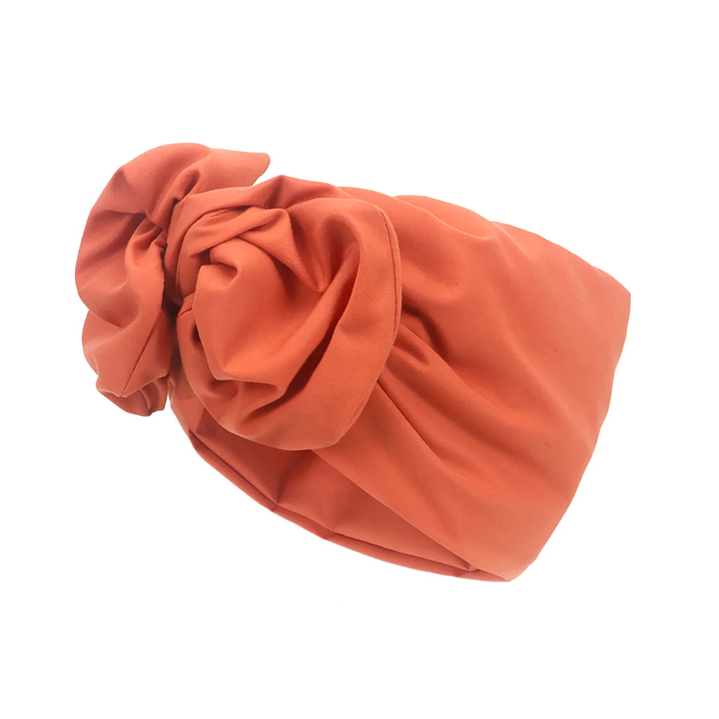 A vintage-style terracotta turban hat featuring a decorative knotted front detail in a soft, matte fabric.