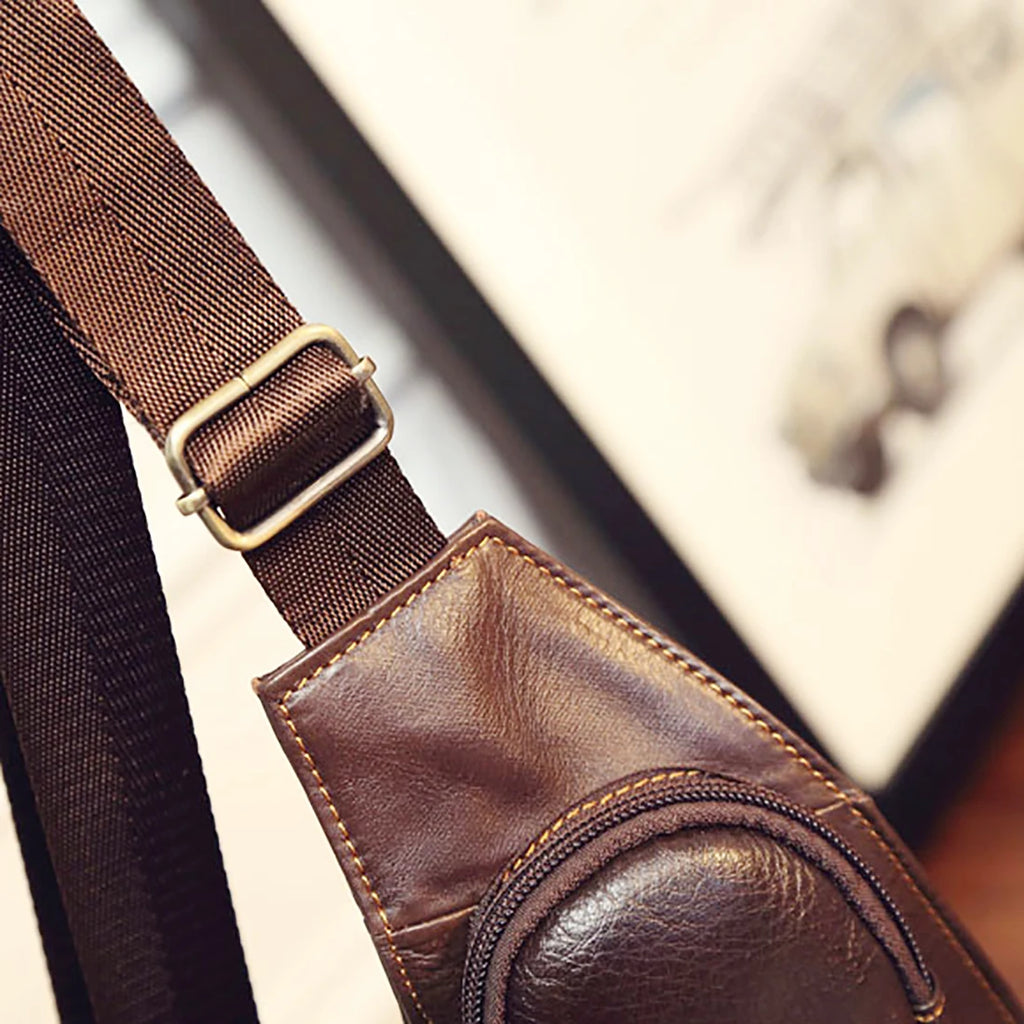 Close-up of a brown leather crossbody sling bag featuring an adjustable strap with a metal buckle and zip detail.