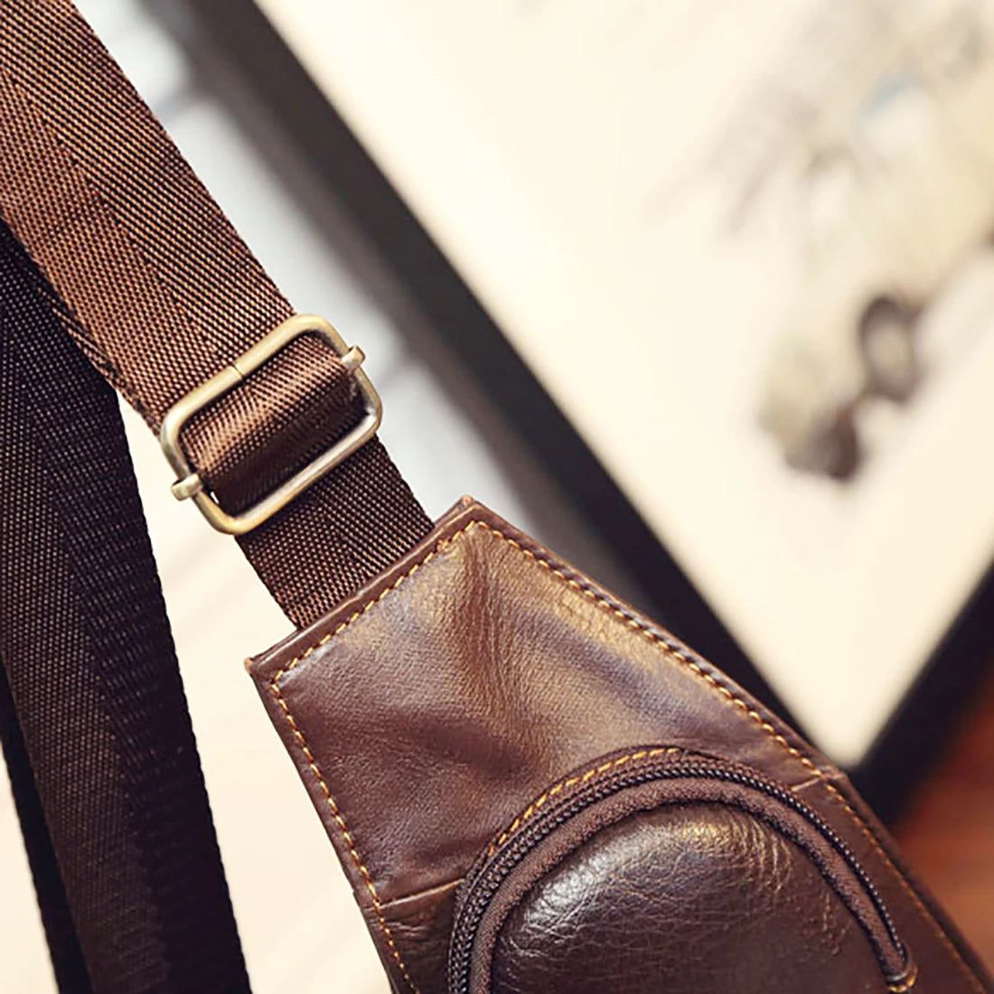 Close-up of a brown leather crossbody sling bag featuring an adjustable strap with a metal buckle and zip detail.