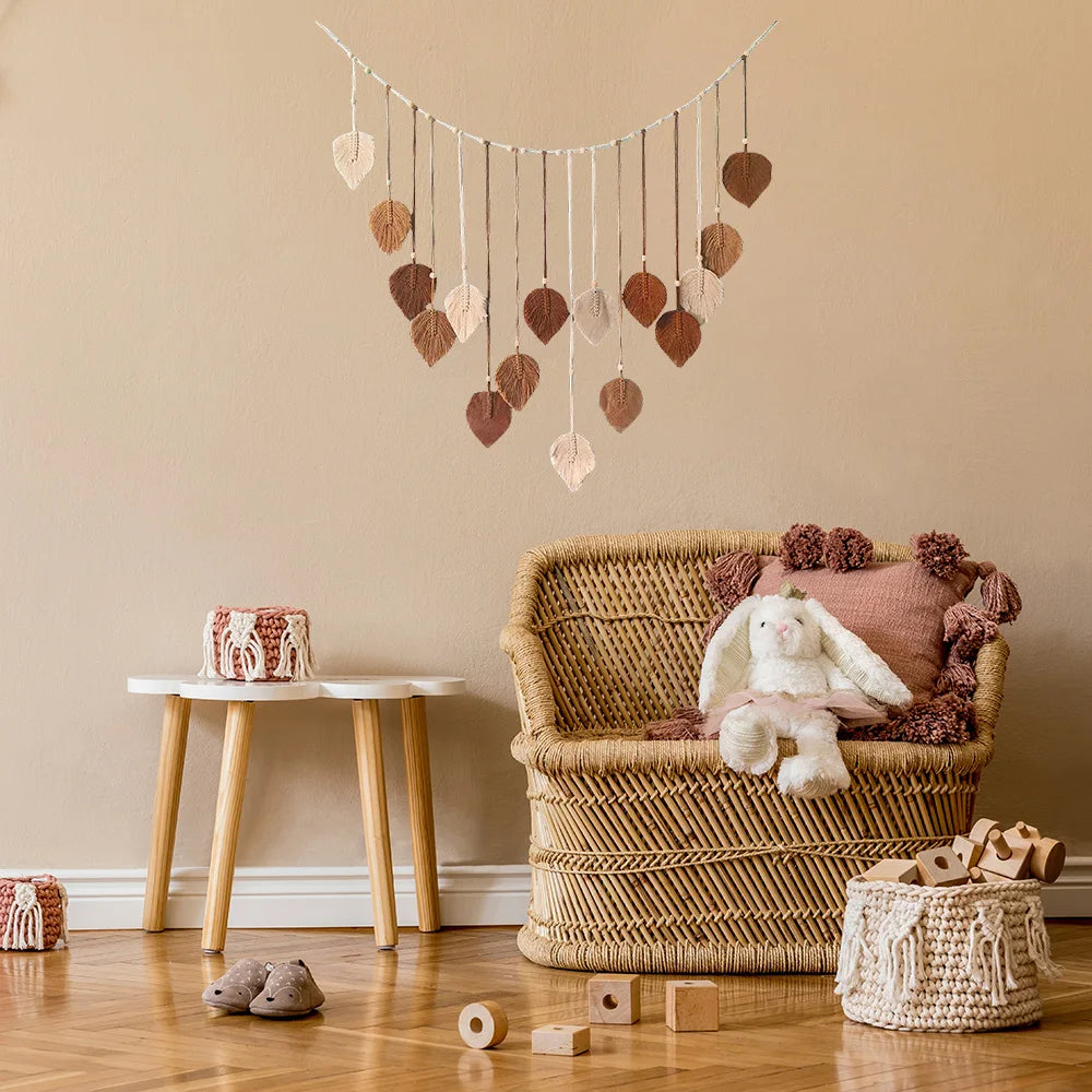 Boho macrame wall hanging featuring hanging leaf-shaped pendants in earthy shades of cream, beige, and terracotta.