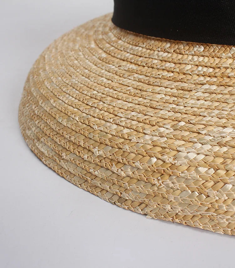 Close-up of a natural woven straw sun hat featuring a wide brim and a contrasting black ribbon band.