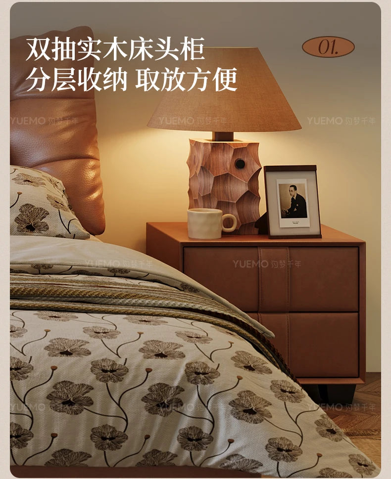 Modern Nordic-style bedside table in tan leather with two drawers, featuring a textured lamp and floral bedding.