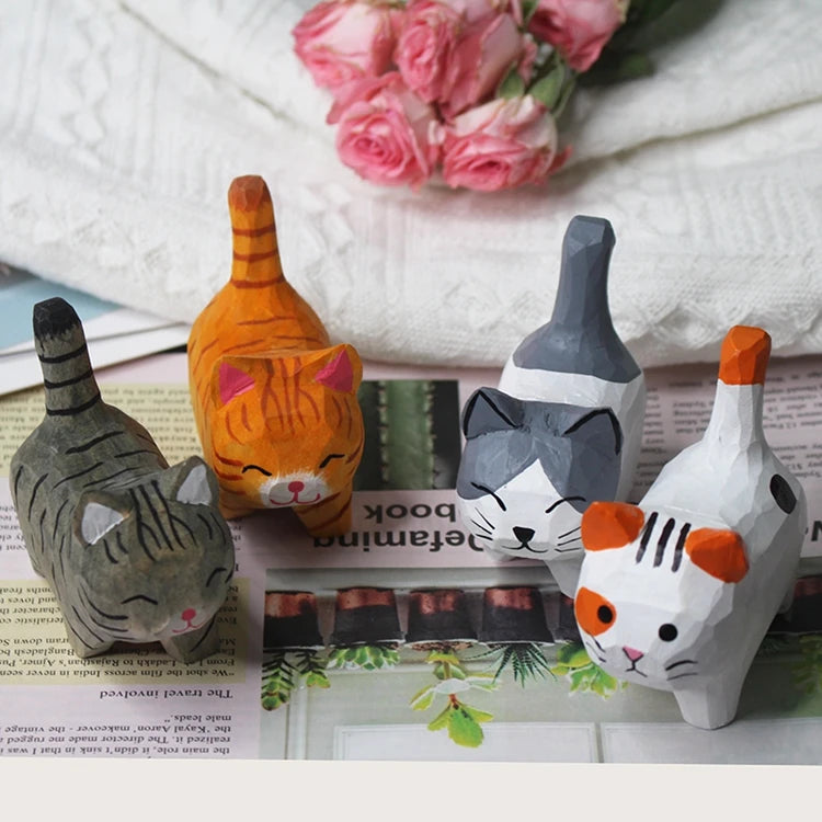 Four handcrafted wooden cat figurines with colourful painted details, displayed on a printed page with pink flowers.