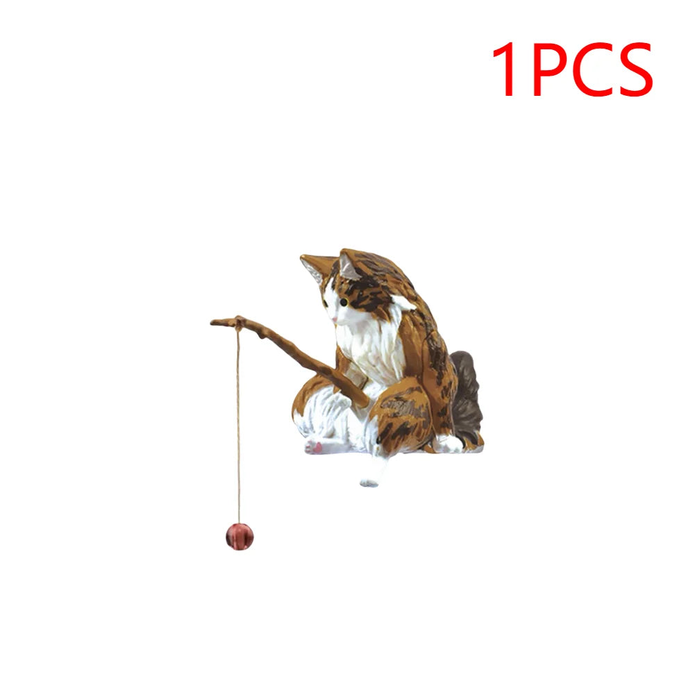 Small brown and white tabby cat aquarium ornament holding a tiny wooden fishing rod with a red baited line.
