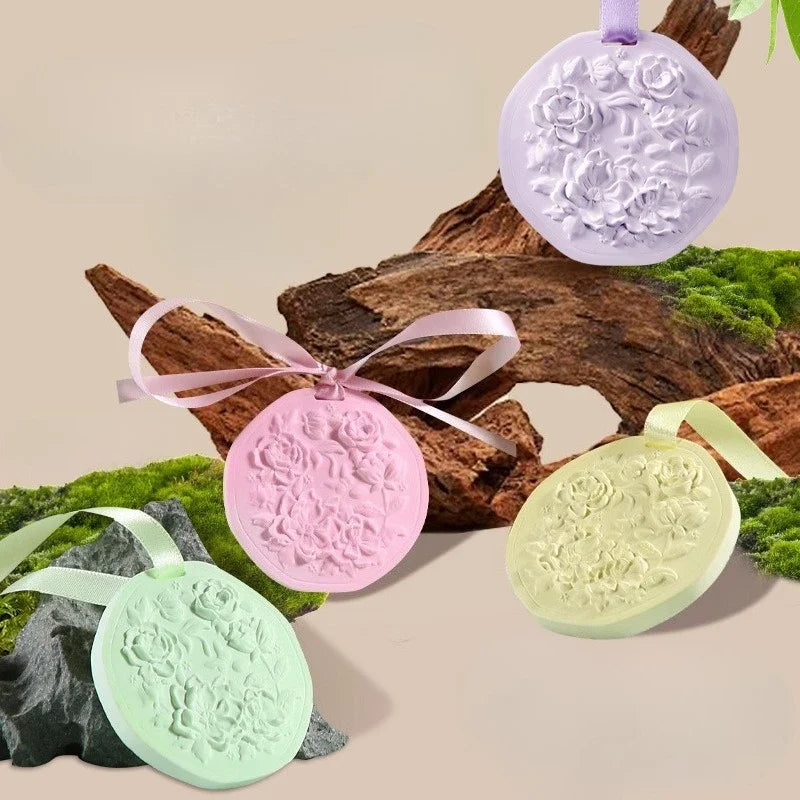 Four round pastel wax tablets in purple, pink, yellow, and green, each featuring a floral relief and ribbon for hanging.