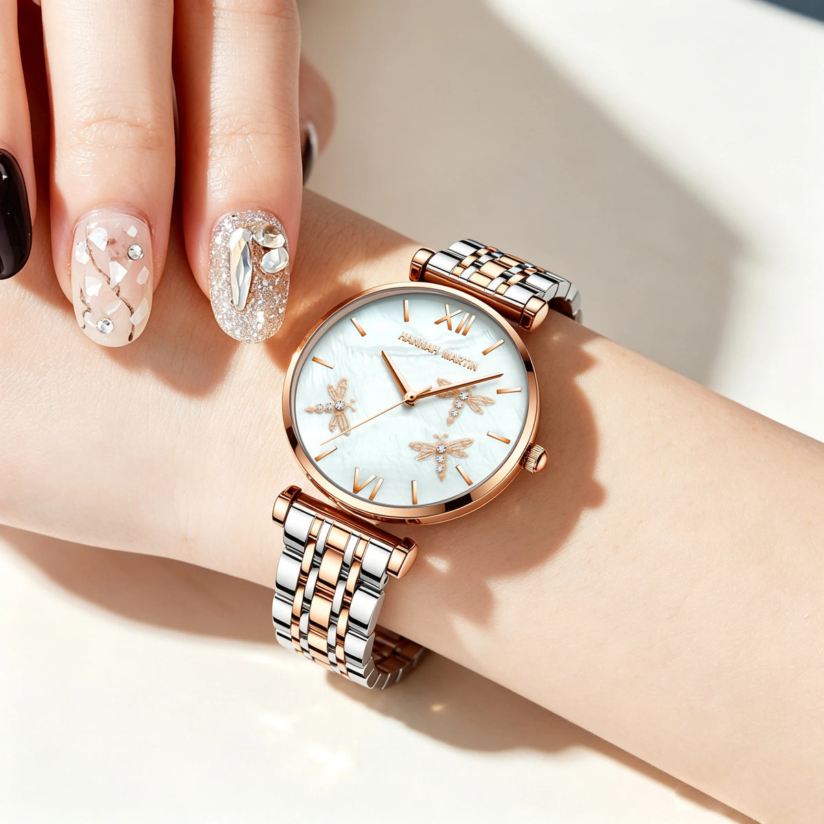 Hannah Martin rose gold and silver watch with mother-of-pearl dragonfly dial and metal link bracelet worn on wrist.