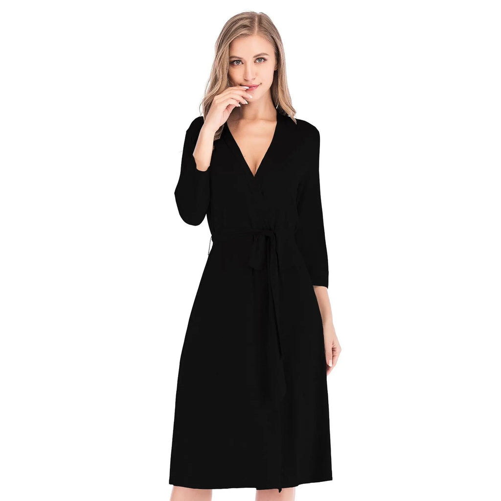 Woman wearing a black midi-length wrap dress with long sleeves and a tie-waist belt against a white background.