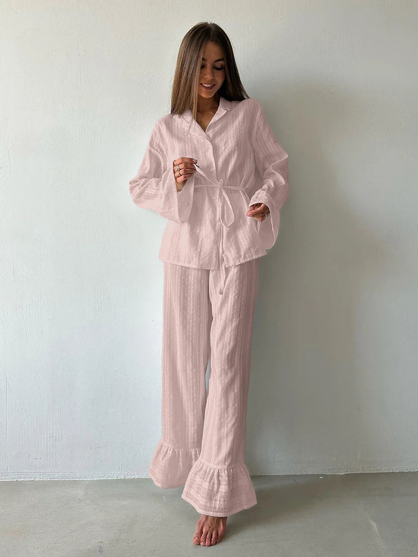 Woman wearing a pale pink, textured two-piece loungewear set with a button-up belted shirt and ruffled wide-leg trousers.