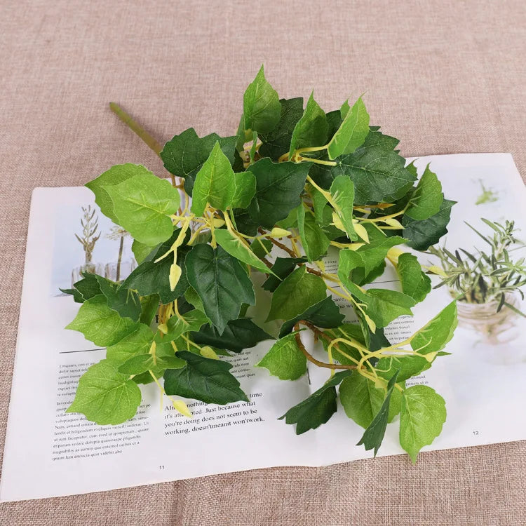 A faux plant stem with variegated light and dark green leaves on yellow-green branches, resting on a printed page.