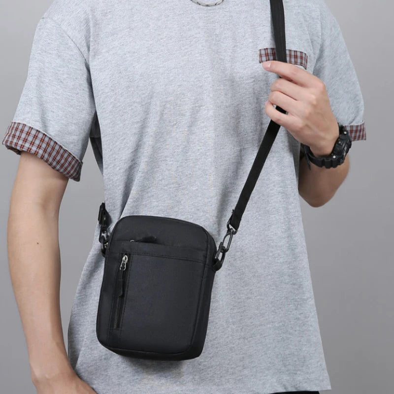A man wearing a compact black crossbody shoulder bag with a zipped front pocket and adjustable shoulder strap.