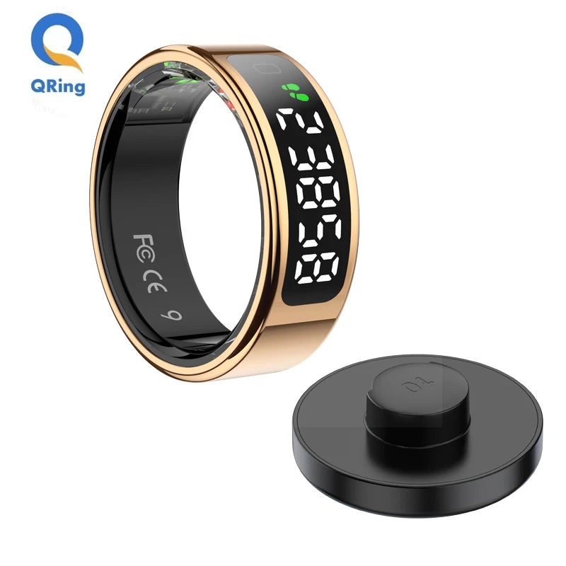 Gold smart fitness ring with a black digital touchscreen display, shown alongside a circular magnetic charging dock.