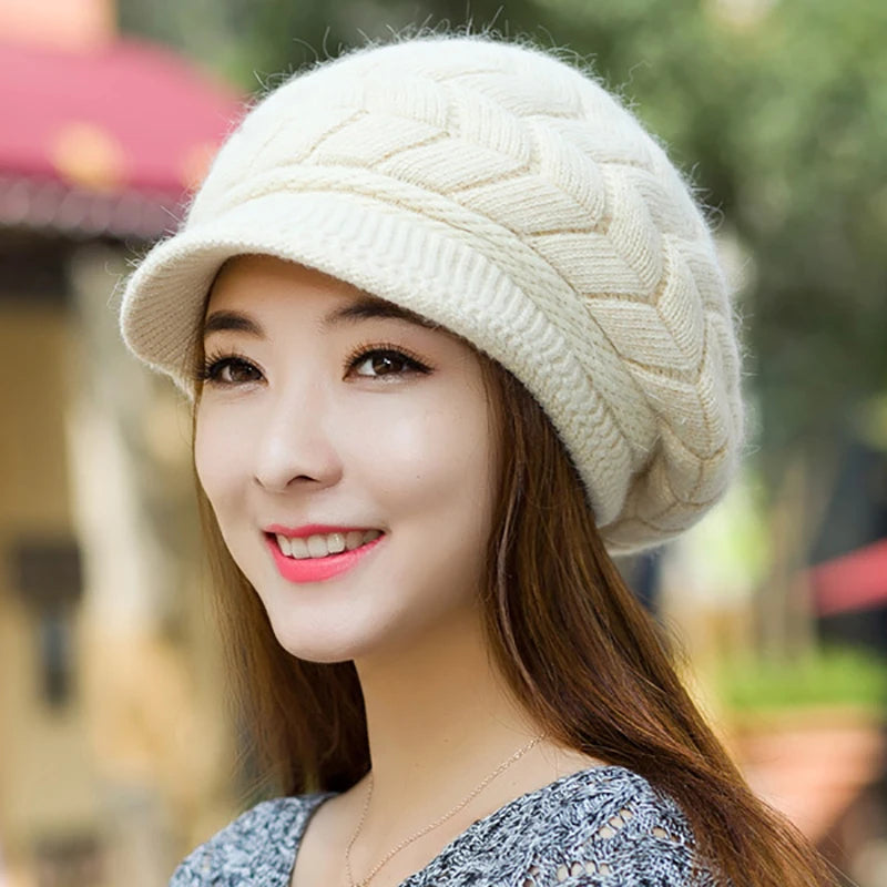 Cream-coloured knitted winter cap with a peak and chevron pattern, worn by a smiling woman.