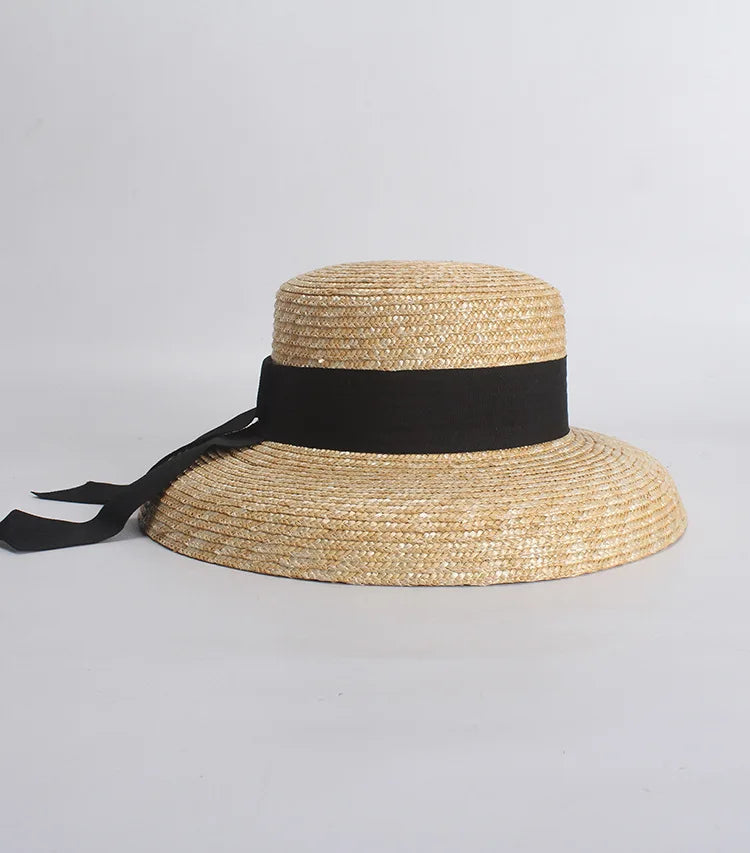 Elegant straw sun hat with a wide brim, flat crown, and a black ribbon band tied in a bow at the side.