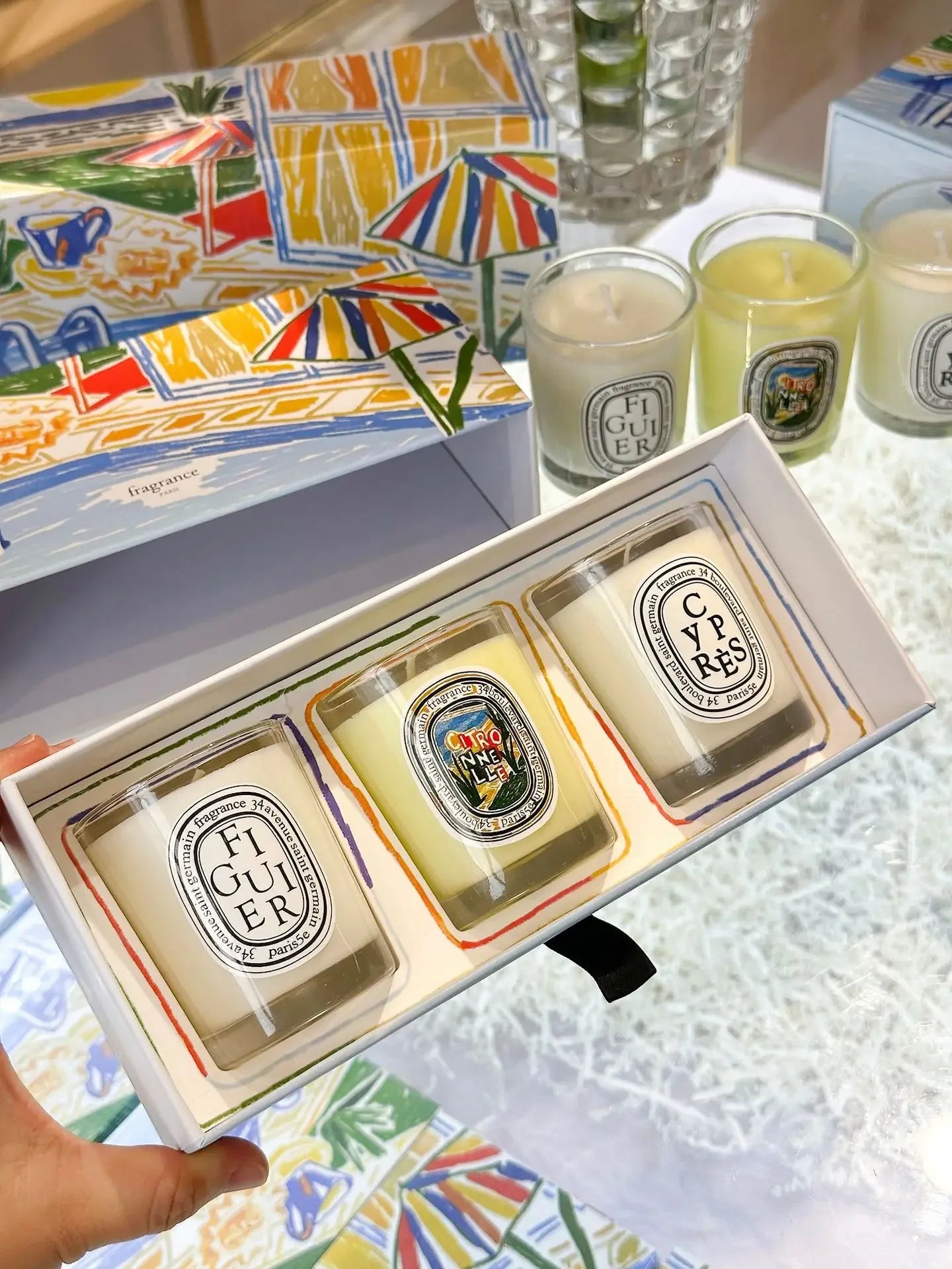 Set of three small scented candles in clear glass jars with illustrated labels, presented in a colourful gift box.