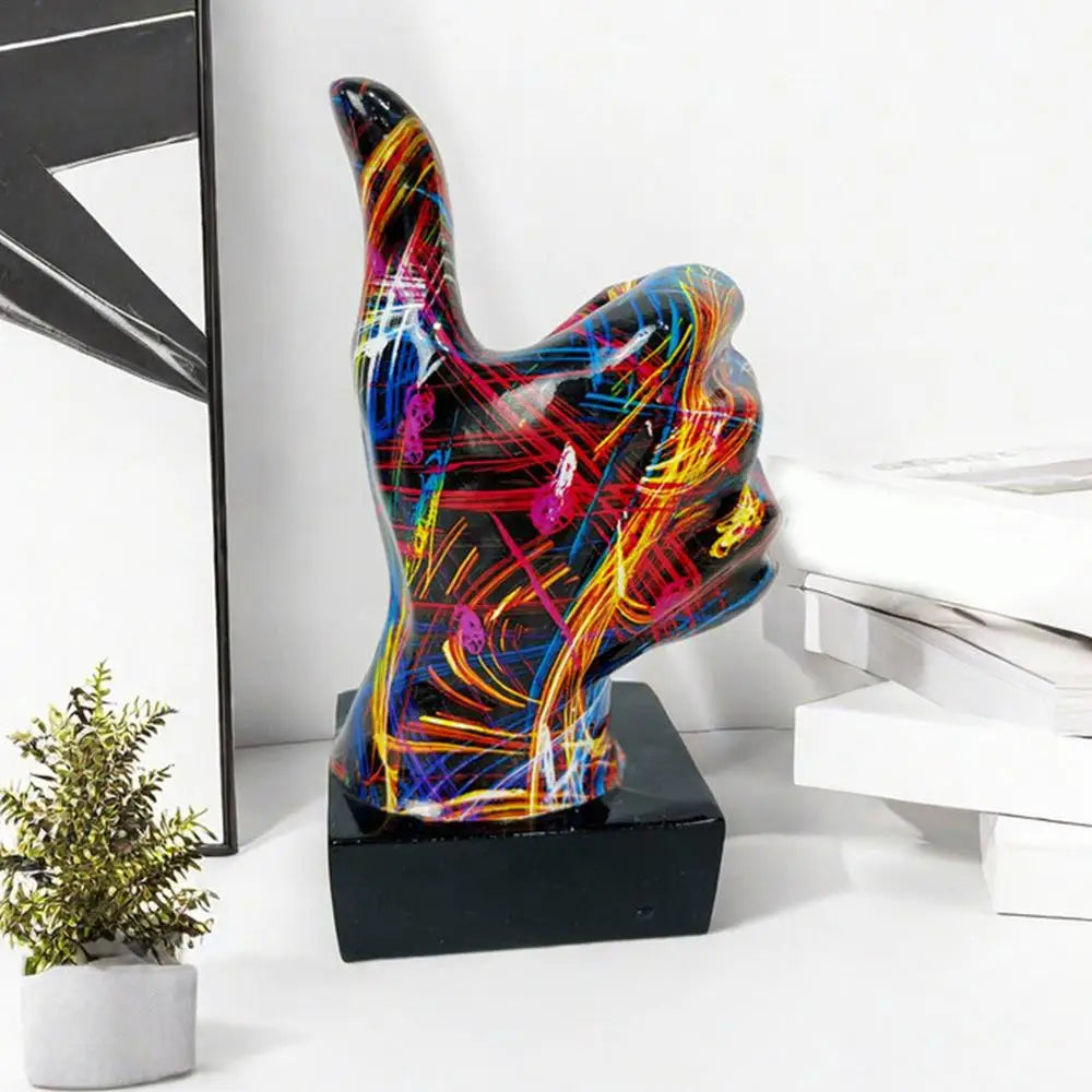 Thumbs-up hand gesture ornament with a colourful, abstract graffiti-style paint design on a black square base.