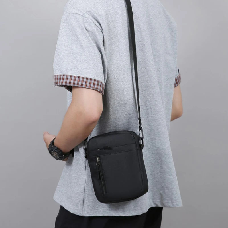 A person wearing a sleek black, durable crossbody bag with an adjustable strap and front zip pocket.