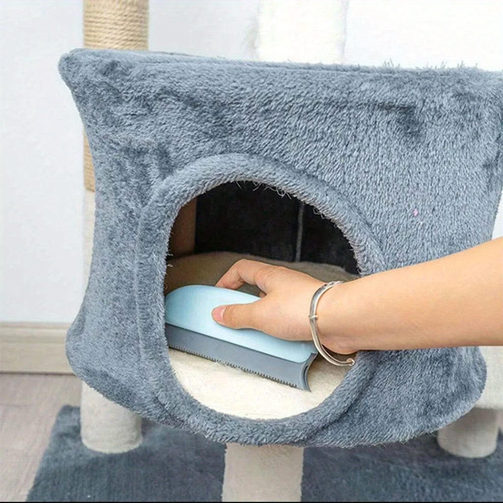 A hand uses a light blue lint remover tool to clean hair from a soft, grey plush cat tree condo.
