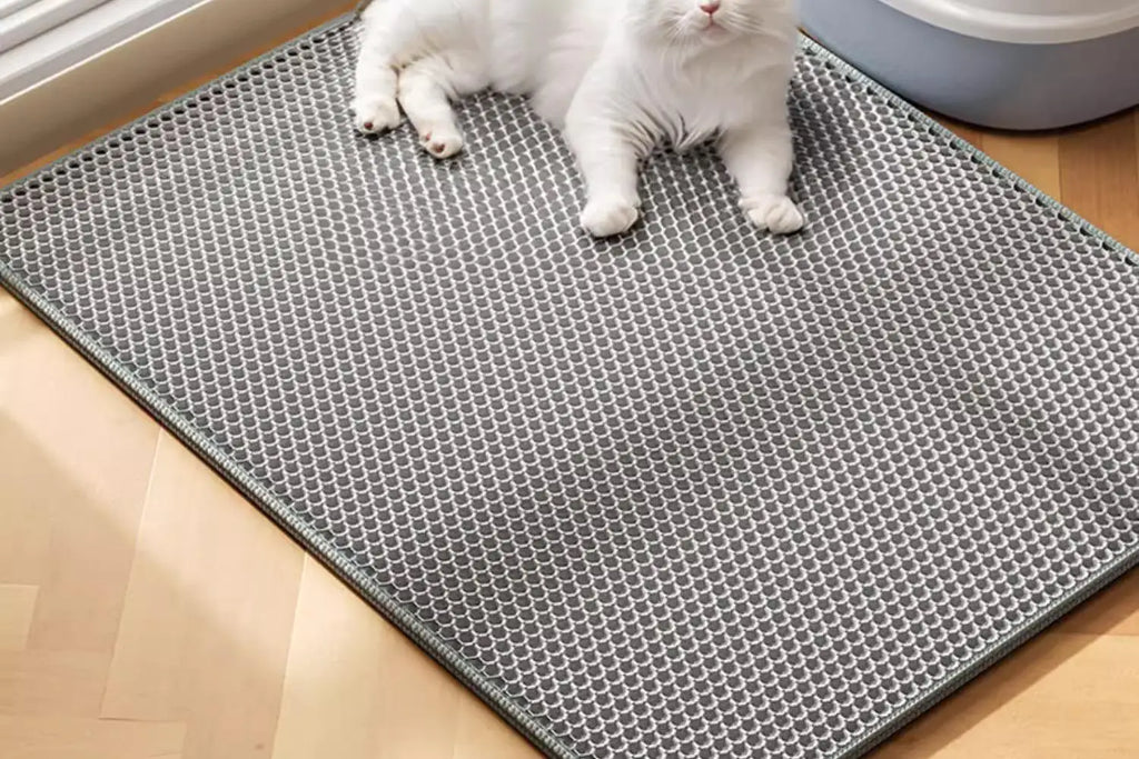 Grey, honeycomb-patterned waterproof cat litter mat on a wooden floor, with a white cat lying on top.