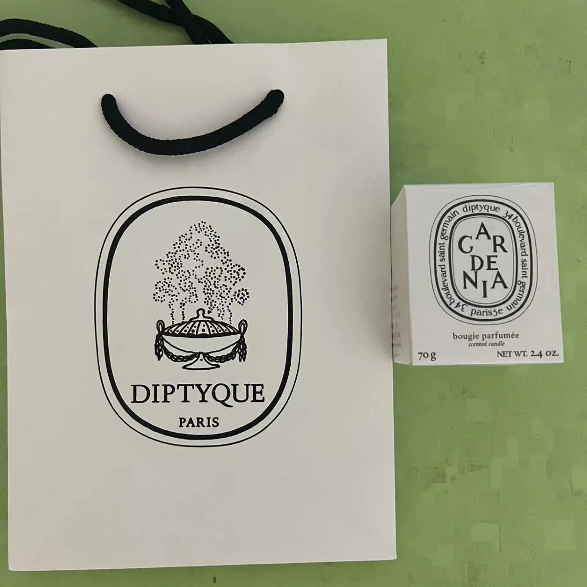 White gift bag with black handles and a small white boxed gardenia scented candle.