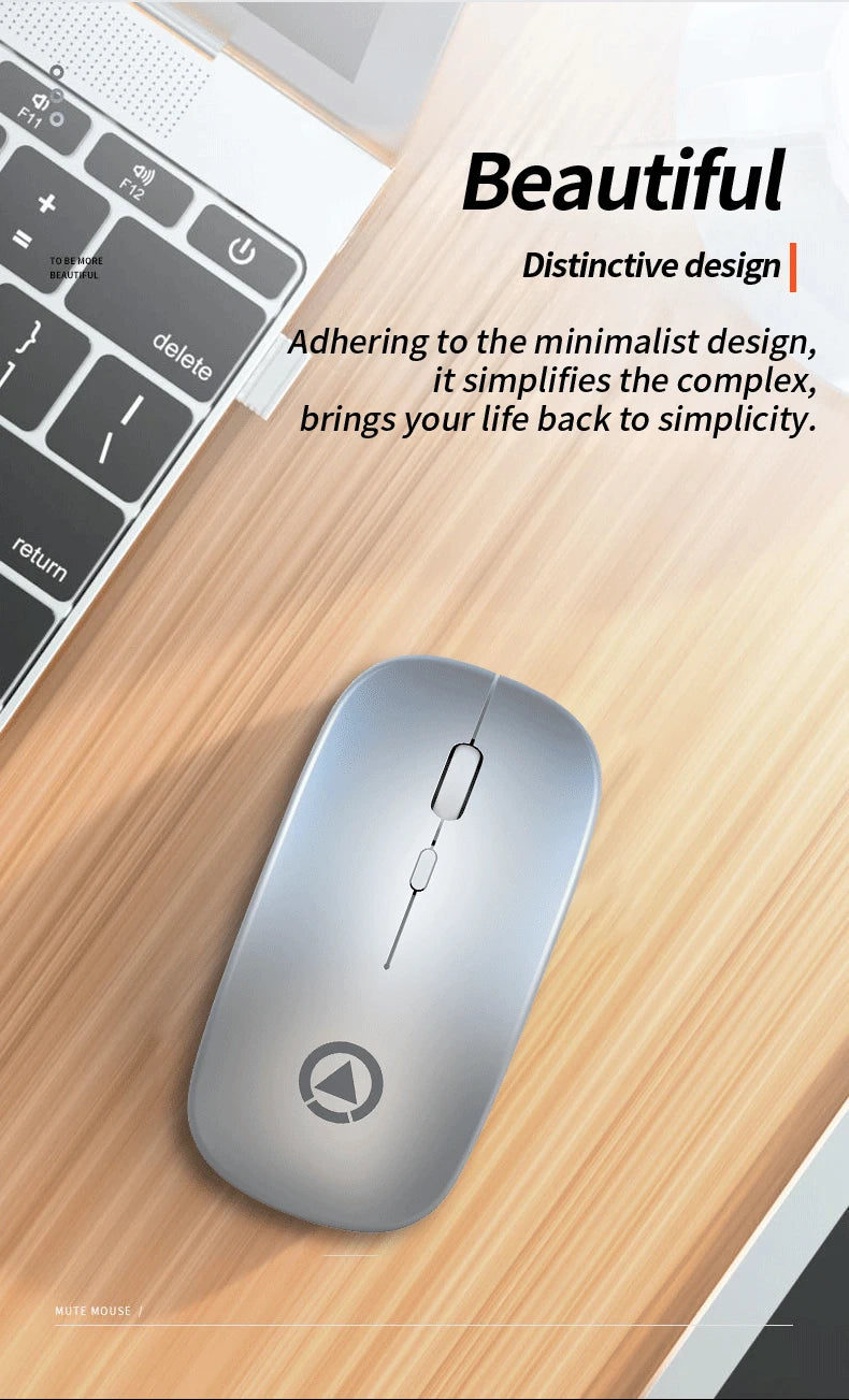 Sleek, silver wireless mouse with a slim, minimalist ergonomic design, resting on a wooden desk next to a laptop.