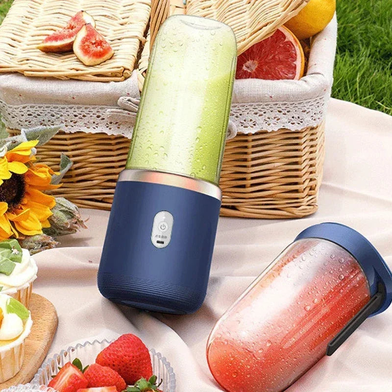 Portable blue personal blender with a clear cup, standing on a picnic blanket with fruit and a basket.