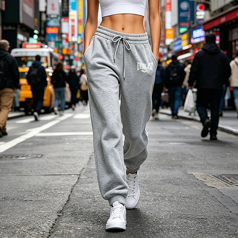Grey high-waisted joggers with a drawstring waist and side pockets, worn with white sneakers on a city street.